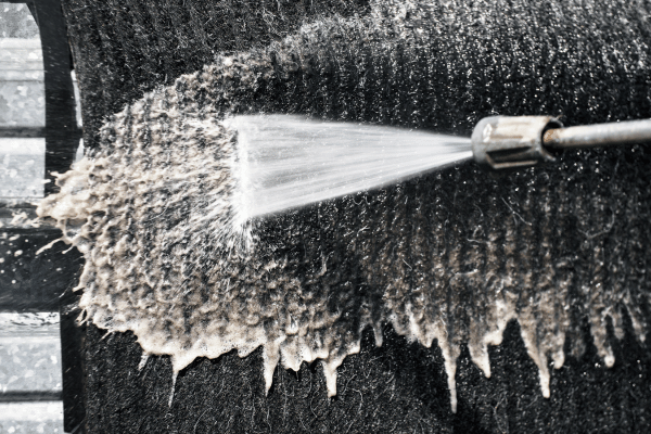 A high-pressure water spray being used for deep cleaning a dark-colored carpet, removing dirt and grime effectively.