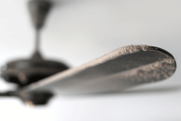 A close-up view of a dusty ceiling fan blade covered in thick layers of dust.