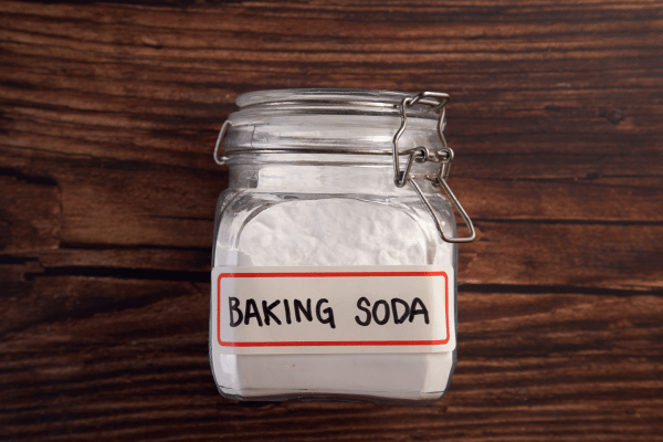 A glass jar labeled "Baking Soda" filled with white powder sits on a wooden surface.