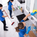 A team of cleaners working in a modern kitchen, wiping cabinets, mopping the floor, and organizing the space.