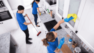 A team of cleaners working in a modern kitchen, wiping cabinets, mopping the floor, and organizing the space.