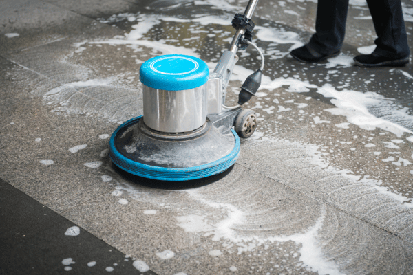 A floor cleaning machine scrubs a tiled surface with soap and water during deep cleaning.

