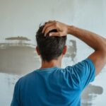 Man in blue shirt worried about dirty, stained wall.