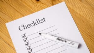 Checklist with checkmarks and whiteboard marker on wooden surface.