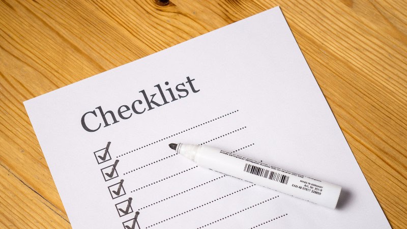 Checklist with checkmarks and whiteboard marker on wooden surface.