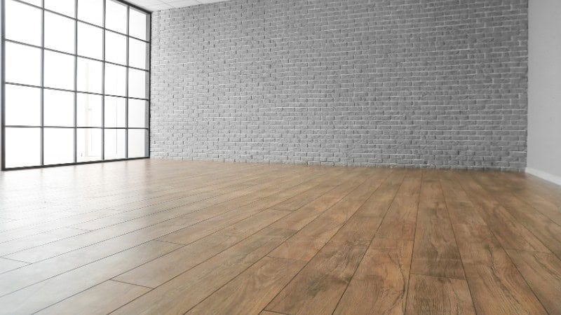 Empty room with laminate floor and brick wall.