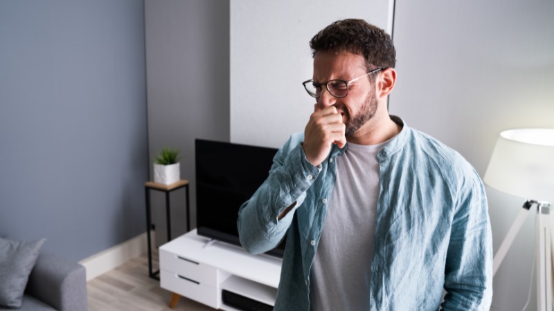 Man covering nose due to odor in modern living room.