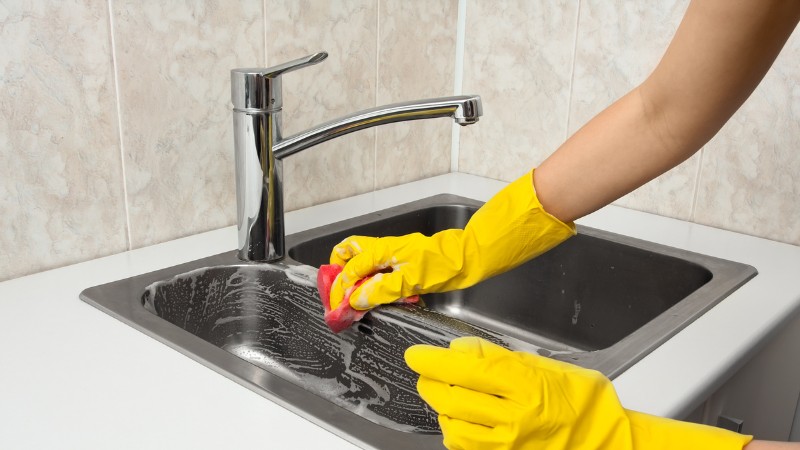 hand with yellow gloves cleaning kitchen sink