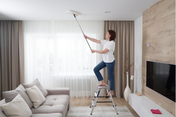 A woman cleaning ceiling in living room with a mop