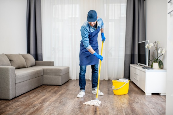 a house cleaner in uniform mopping floor with mop in small living room