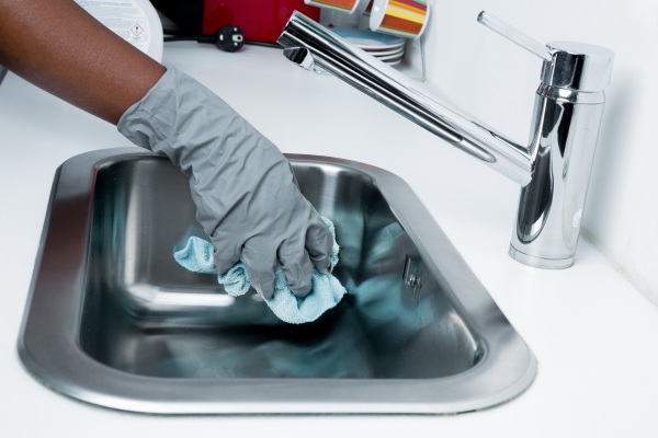 a person is gloved polishing the kitchen sink after cleaning