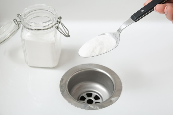 hand pouring one spoon of baking soda inside the kitchen sink drain