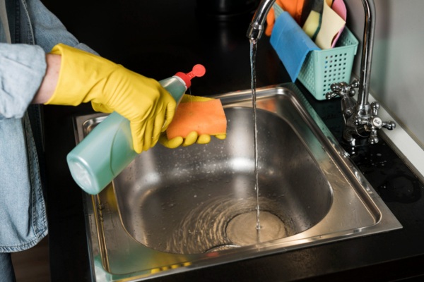 a person with yellow gloves rinsing kitchen sink before cleaning it