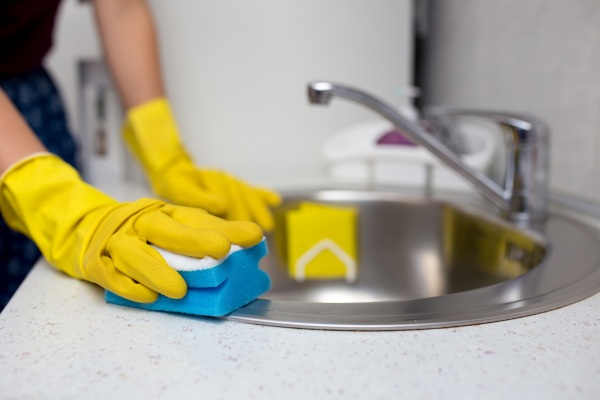 a person with yellow gloved rubbing the kitchen sink with sponge