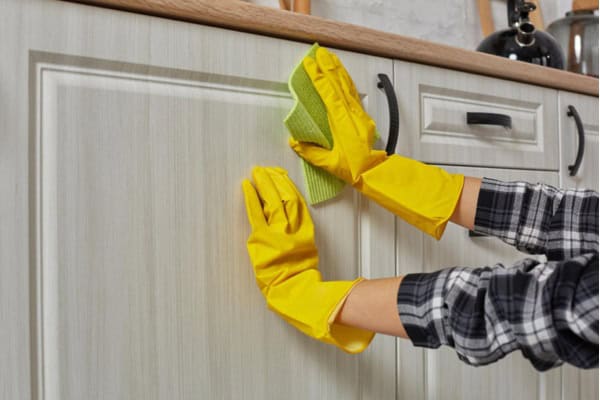 hand in yellow gloves wiping kitchen cabinet