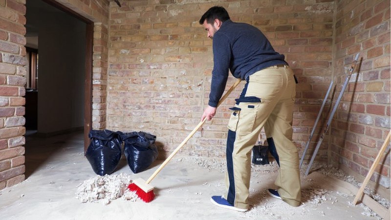 Worker sweeping construction debris into a pile in an empty room.