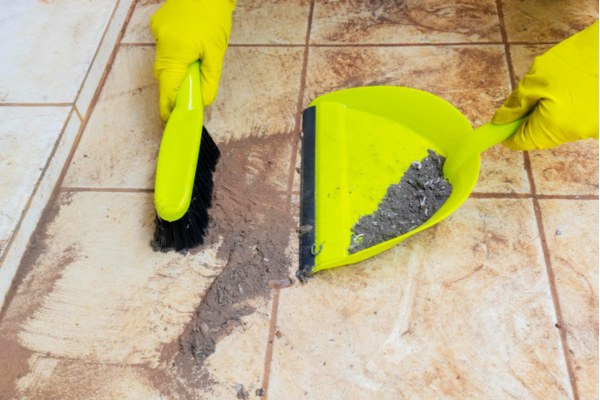 Close-up of hands sweeping construction dust into dustpan on tile floor.