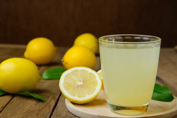 Glass of fresh lemon juice with whole and sliced lemons on table.
