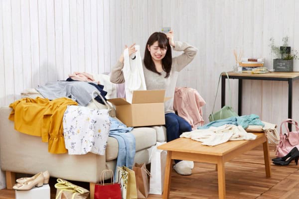 Woman stressed while sorting cluttered clothes in messy room.