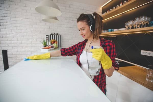 Young woman wearing headphones happily cleaning kitchen counter.