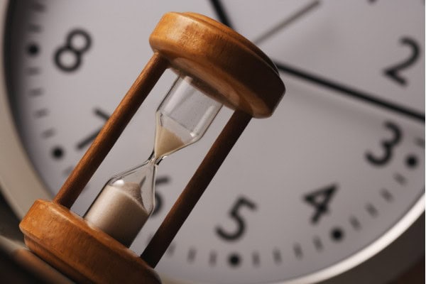 Close-up of hourglass in front of clock showing time passing.