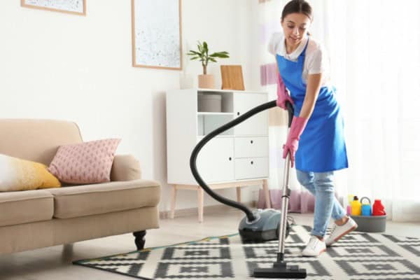 Maid vacuuming patterned carpet in bright living room