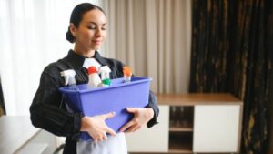 Maid holding blue container filled with cleaning spray bottles