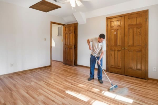Man sweeping dust off linoleum floor in empty room.