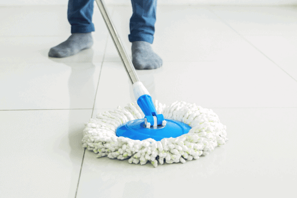 Person mopping a shiny white tile floor with a blue spin mop.