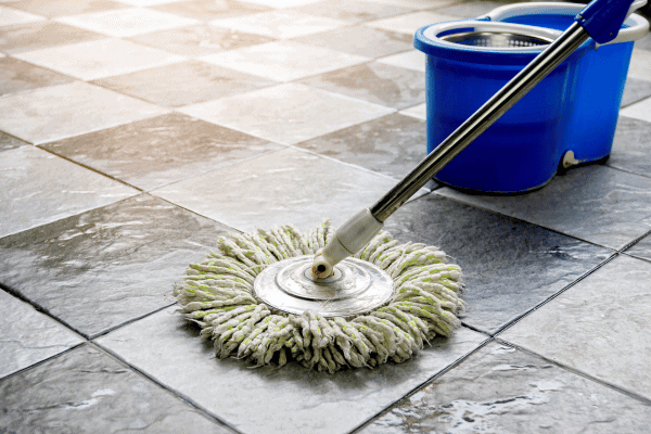 Spin mop cleaning patterned gray tile floor beside blue bucket.